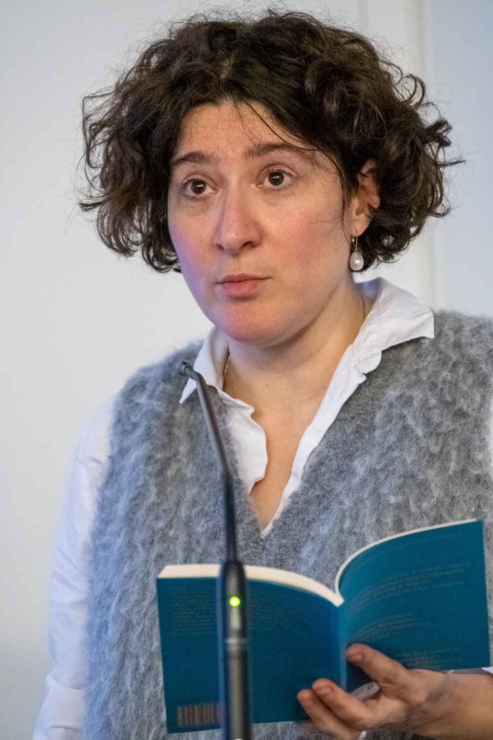 Zielinski.Photography - Images of artworks and culture - Berlin A woman holding a book and speaking into a microphone, capturing a moment of literature and artistry through photography.