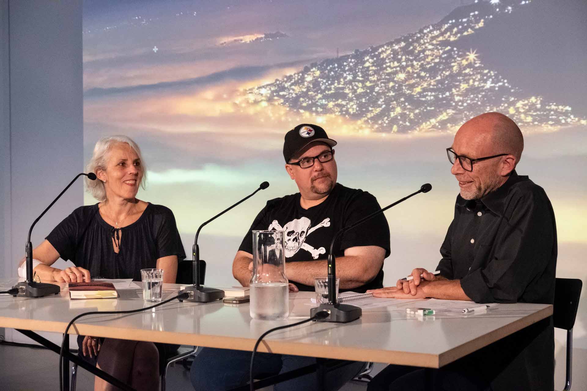Zielinski.Photography - Images of artworks and culture - Berlin Three people sitting at a table in front of a projection screen, engrossed in literature.