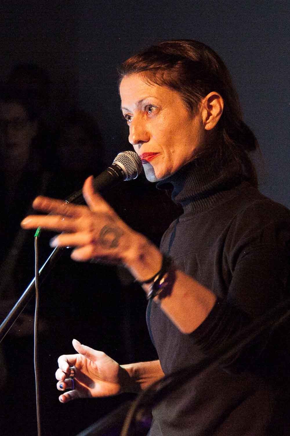 Zielinski.Photography - Images of artworks and culture - Berlin A woman delivering a literature performance while speaking into a microphone in front of a crowd, showcasing her artworks.