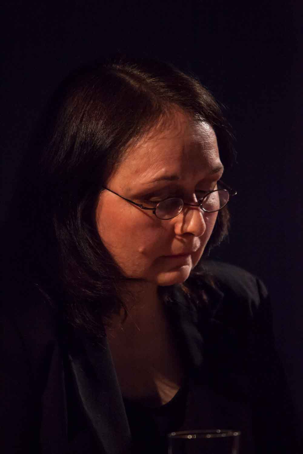 Zielinski.Photography - Images of artworks and culture - Berlin A woman in glasses sitting at a table with a glass of wine, engrossed in literature.