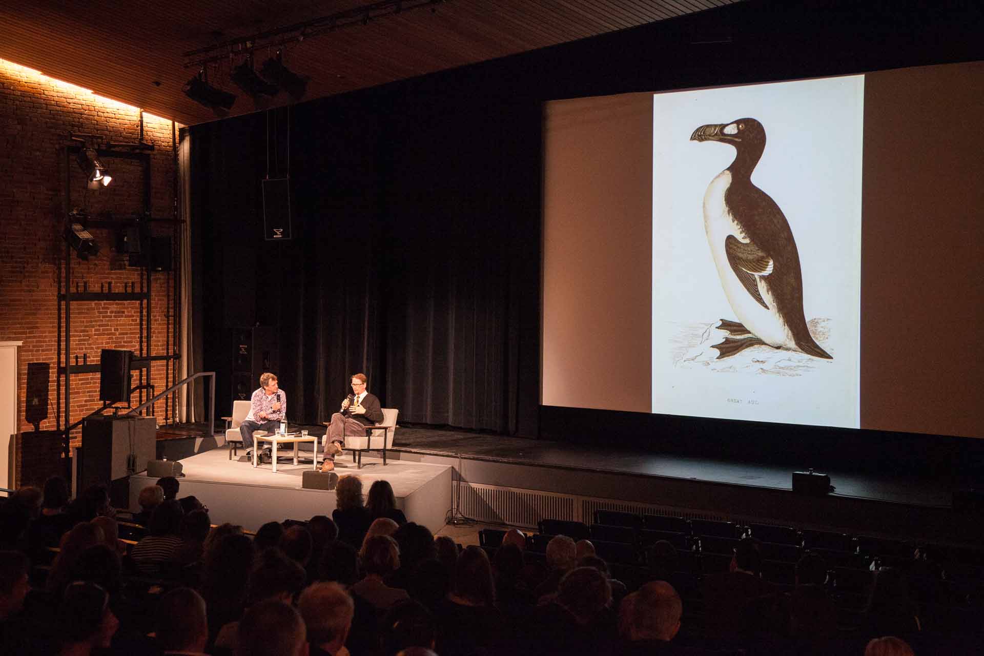 Zielinski.Photography - Images of artworks and culture - Berlin A group of people sitting in front of an image of a penguin during a performance by Zielinski.