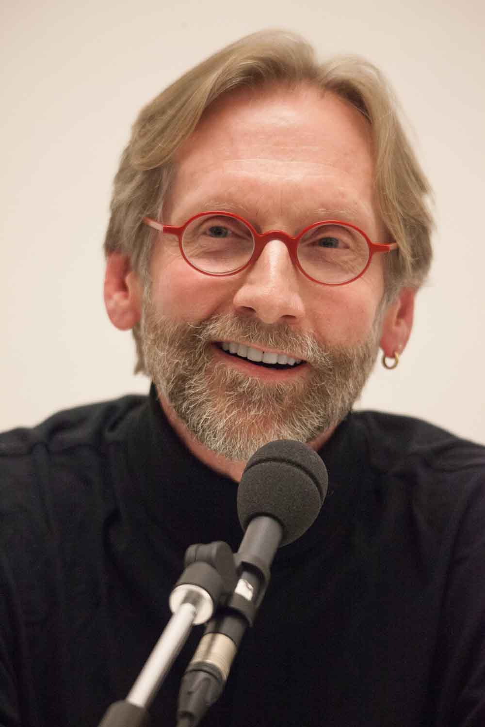 Zielinski.Photography - Images of artworks and culture - Berlin A man with glasses and a beard giving a performance at a microphone, showcasing his literary artworks.