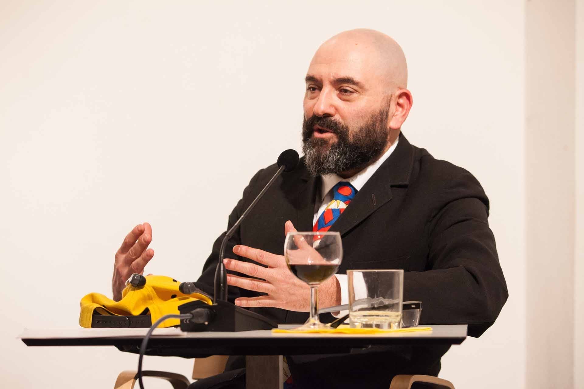 Zielinski.Photography - Images of artworks and culture - Berlin A bald man in a suit giving a literature performance while speaking into a microphone.