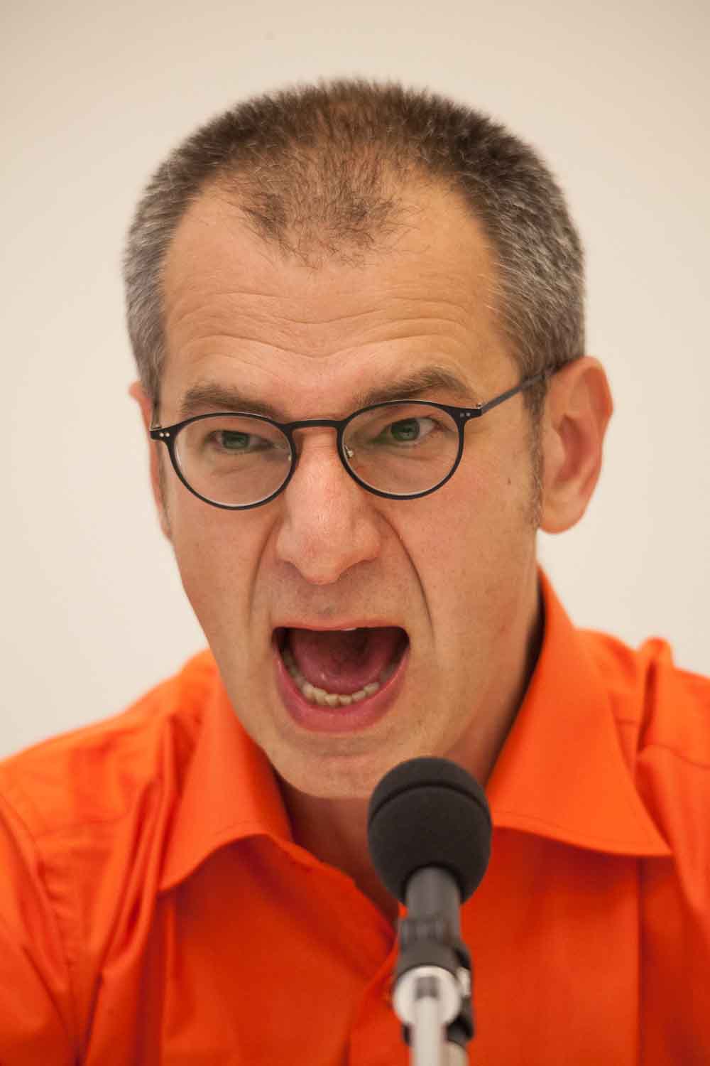 Zielinski.Photography - Images of artworks and culture - Berlin A man in an orange shirt is passionately shouting into a microphone during a performance.