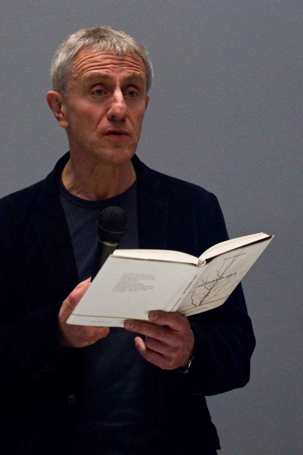 Zielinski.Photography - Images of artworks and culture - Berlin A man giving a performance by holding a book and speaking into a microphone at an exhibition of artworks.