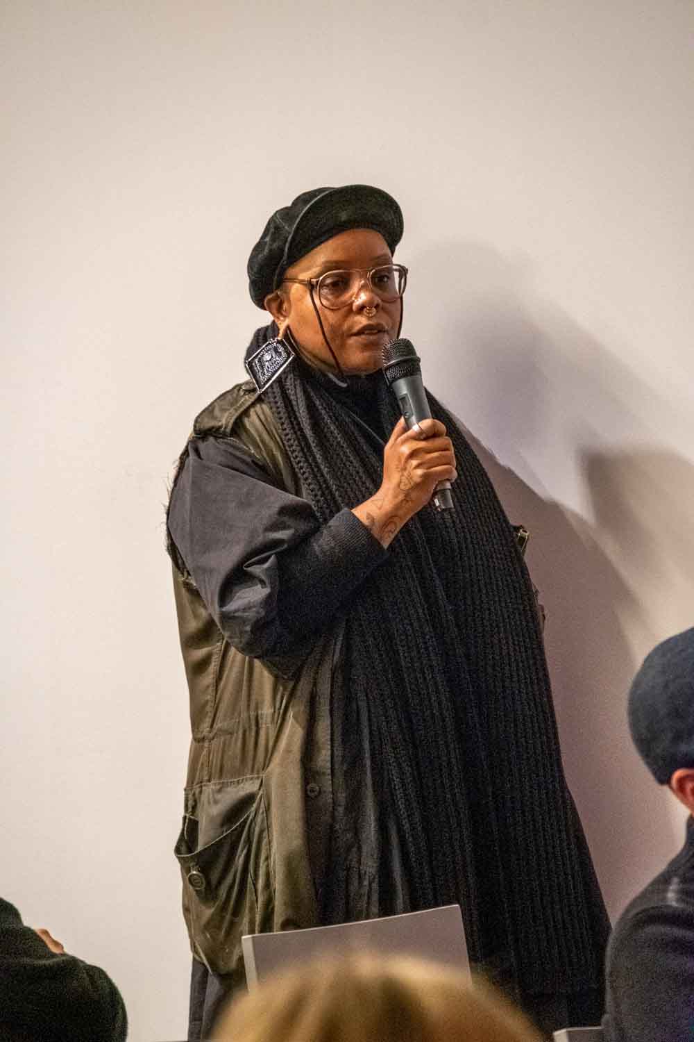Zielinski.Photography - Images of artworks and culture - Berlin A woman delivering a powerful speech into a microphone before an attentive audience, capturing the essence of performance art and creating a lasting documentation of the event.