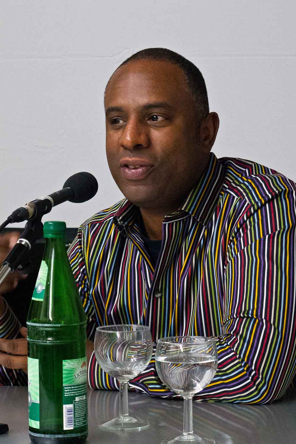 Zielinski.Photography - Images of artworks and culture - Berlin Stan Douglas sitting at a table with a bottle of water and a microphone.